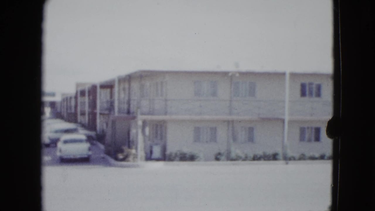 1958 Las Vegas home-movie frame showing a long two-story motel exterior with open walkways and cars at the left edge.