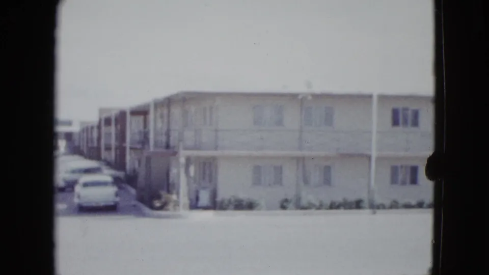1958 Las Vegas home-movie frame showing a long two-story motel exterior with open walkways and cars at the left edge.