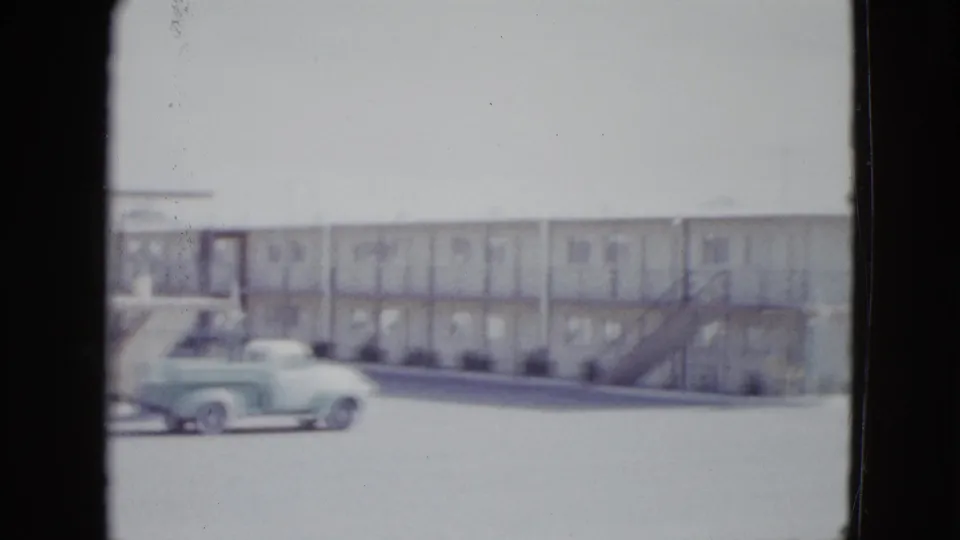 1958 Las Vegas motel frontage with exterior stairs, repeated doors or windows, and the light green pickup low in frame.
