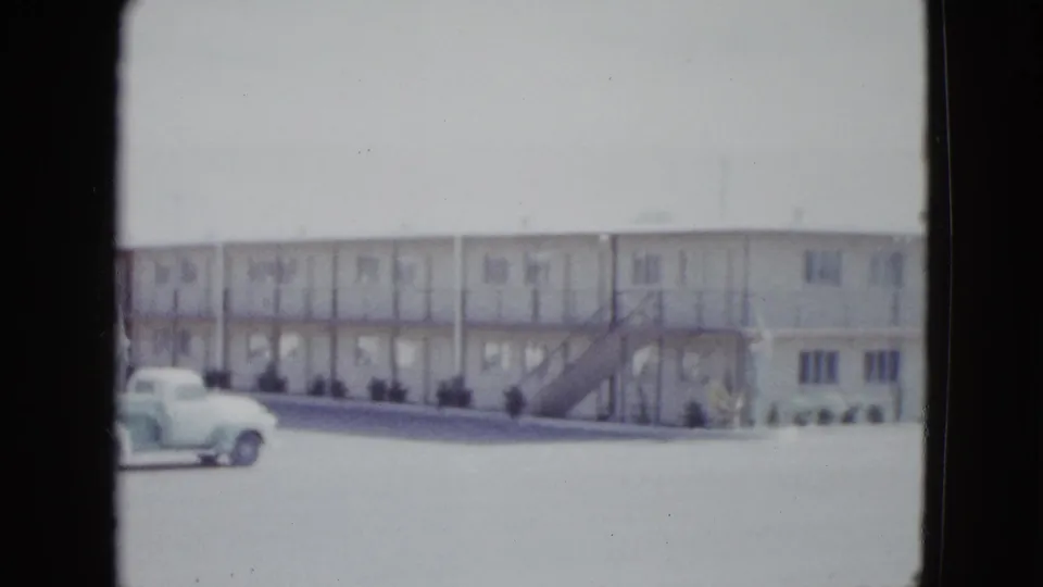 1958 Las Vegas home-movie frame showing a white two-story motel facade with exterior stairs and a light vintage pickup in front.
