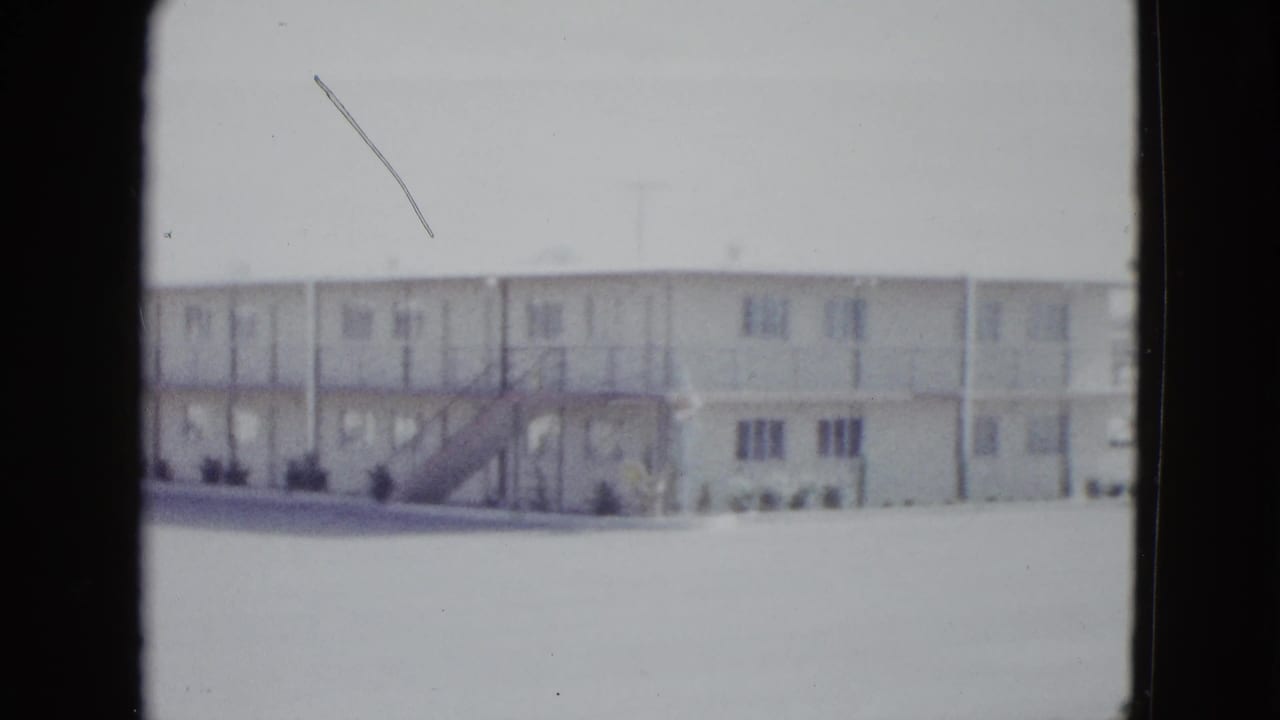 1958 Las Vegas frame of a low-rise white motel building, exterior stairway, repeated rooms, and sparse landscaping.