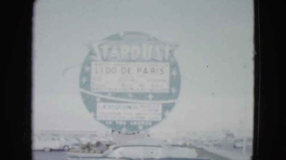 1958 Las Vegas frame showing the Stardust roadside sign with Lido de Paris text, parked cars below, and a bright overexposed sky.