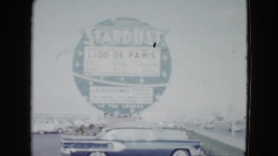 1958 Las Vegas street view with a dark convertible passing beneath the circular Stardust sign advertising Lido de Paris.