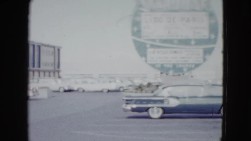 1958 Las Vegas casino exterior with Stardust signage, parked white cars, and a dark convertible in soft color 8mm footage.