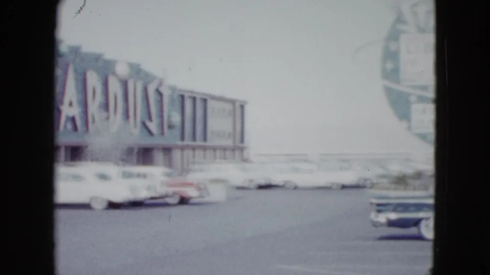 1958 Las Vegas street view with the Stardust facade, several parked cars, and a partial circular sign at the frame edge.