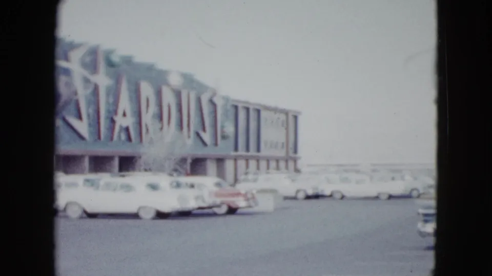 1958 Las Vegas view of the Stardust Hotel sign and parking lot, with mid-century cars in the foreground.