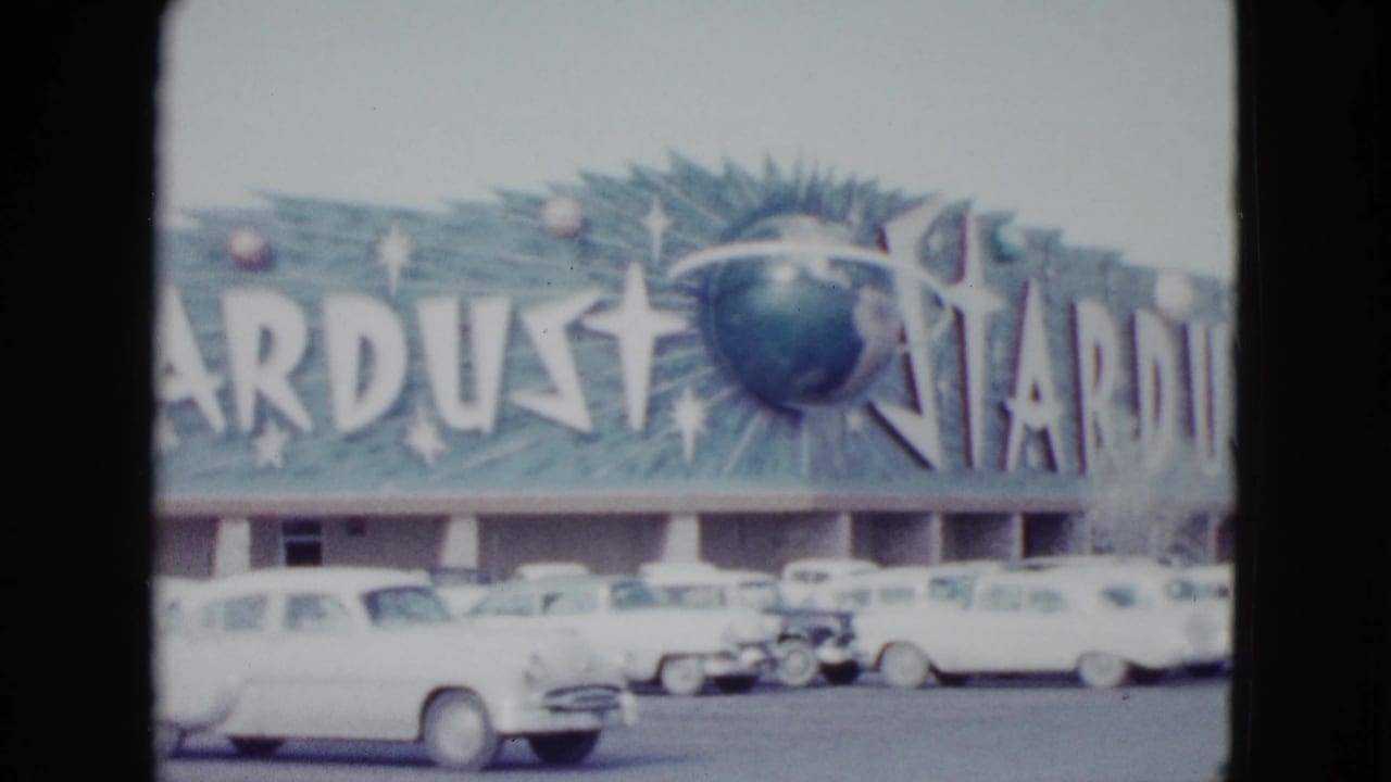 Stardust sign above a motel frontage with late-1950s cars in the parking lot.
