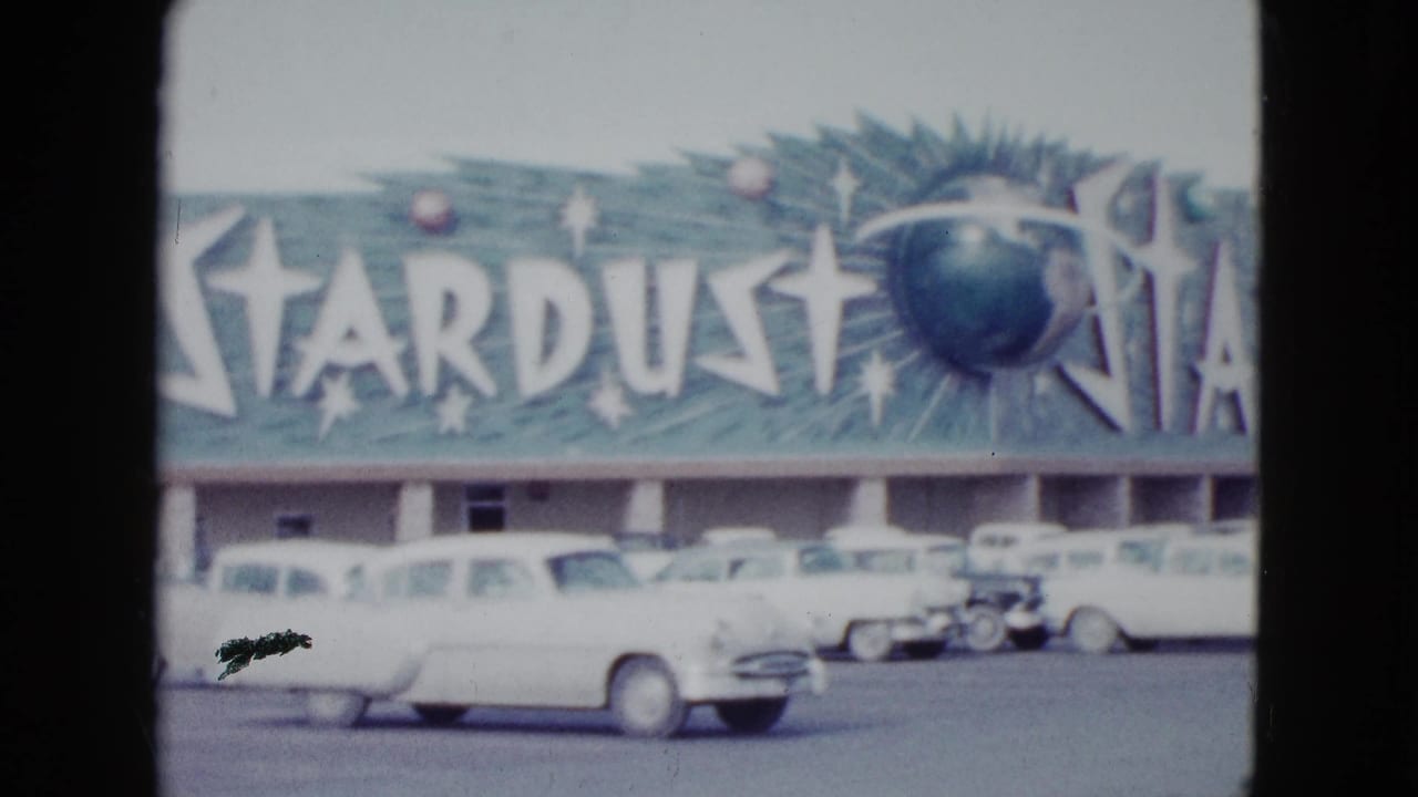 Stardust sign and motel exterior with several white cars parked or passing in front.