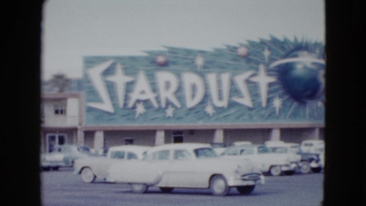 1958 Las Vegas 8mm frame centered on the Stardust sign and motel frontage, with rounded cars in the lot below.