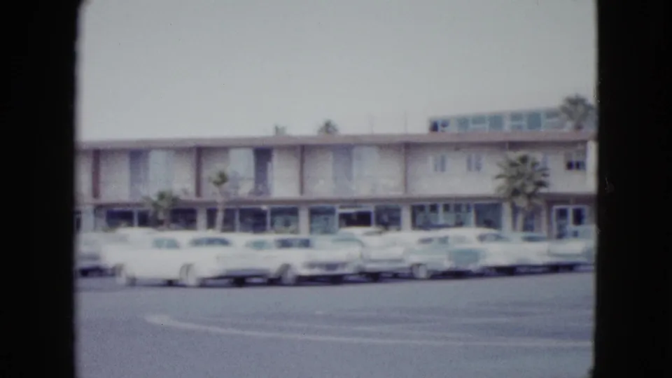 1958 Las Vegas hotel exterior with rows of rounded American cars parked before a low modern facade.