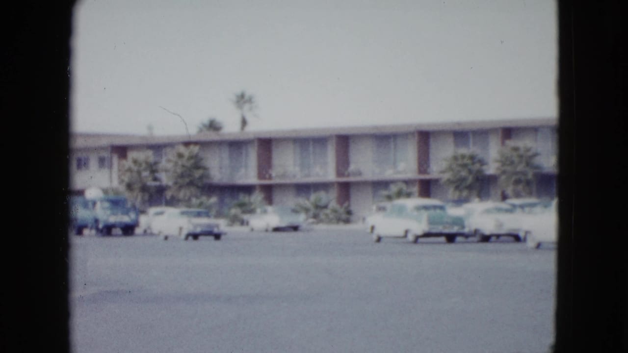 Low-rise motel parking lot with parked cars and palm trees.