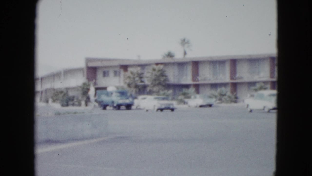 Motel parking lot with a blue truck and light-colored cars near the building.