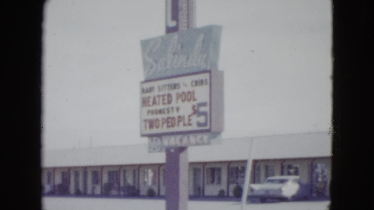 Large motel roadside sign above a long motel building with a parked car.