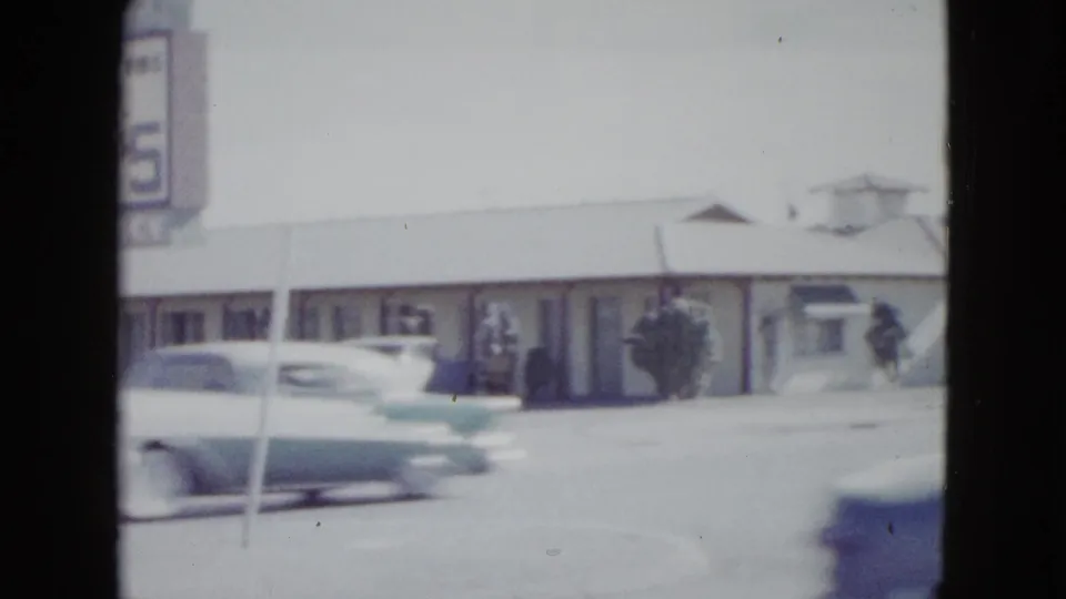 A late-1950s style car passes through the foreground as the Las Vegas motel frontage and partial sign remain visible behind it.
