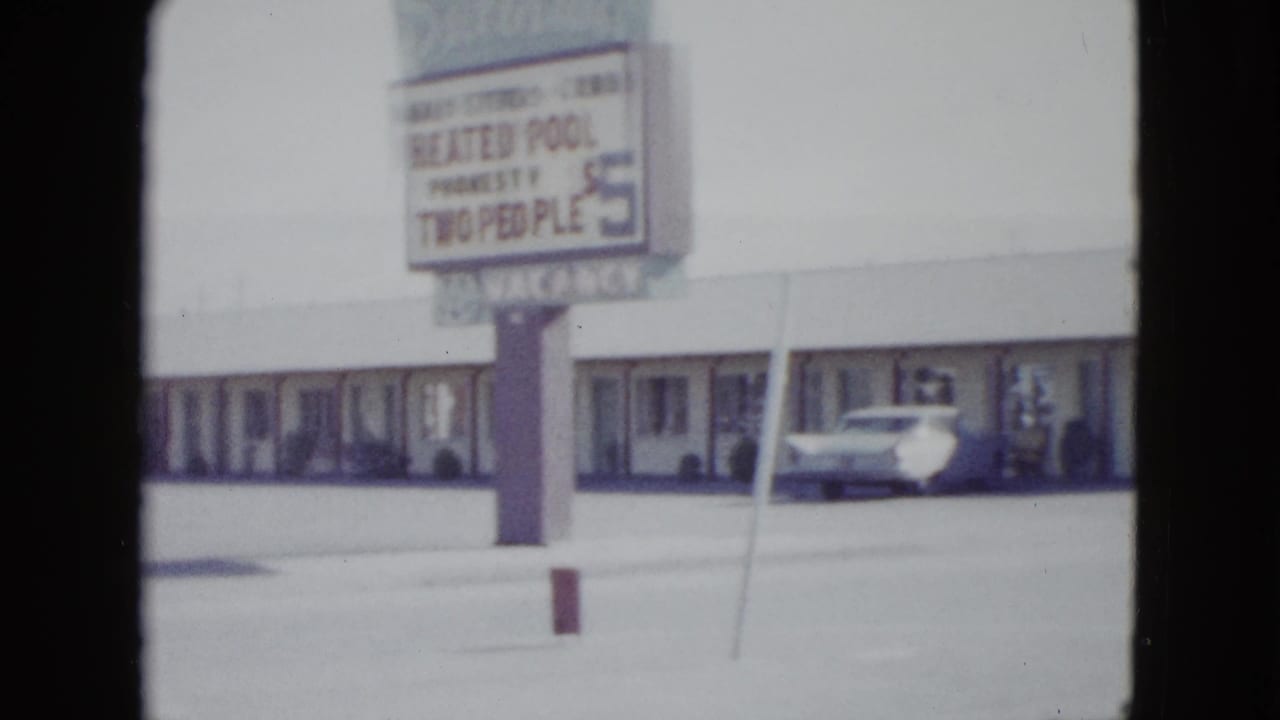 1958 Las Vegas frame with a motel pole sign advertising a heated pool, set before a low roadside lodging building and parked car.