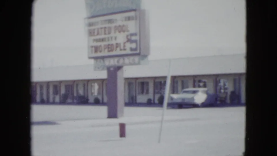 1958 Las Vegas frame with a motel pole sign advertising a heated pool, set before a low roadside lodging building and parked car.