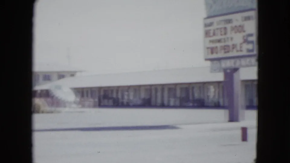 Soft 8mm frame from Las Vegas in 1958 showing a cropped motel sign, low lodging frontage, and open paved foreground.