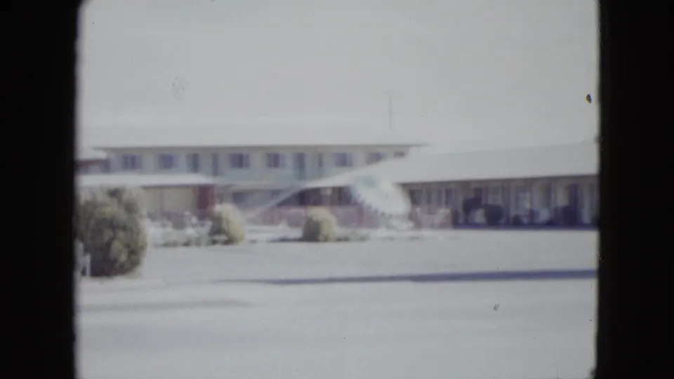 Wide 1958 Las Vegas home-movie view of a single-story motel frontage with shrubs, pavement, and soft faded color.