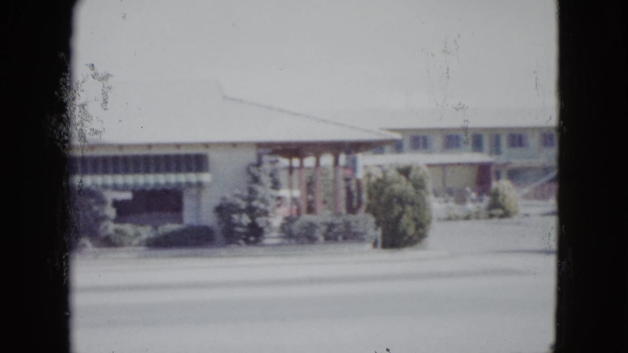 Las Vegas motel exterior in a soft 1958 8mm frame, showing awnings, shrubs, and roadside frontage.