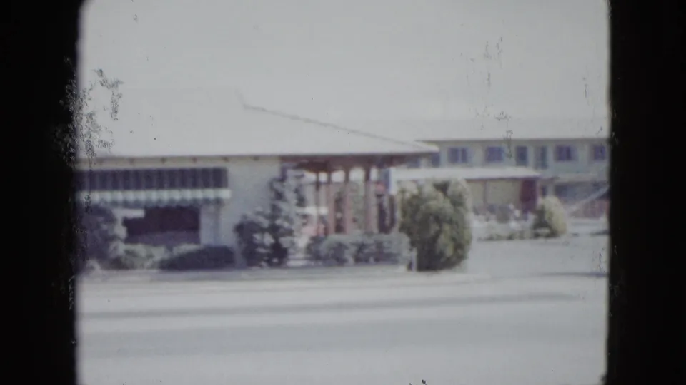 Las Vegas motel exterior in a soft 1958 8mm frame, showing awnings, shrubs, and roadside frontage.