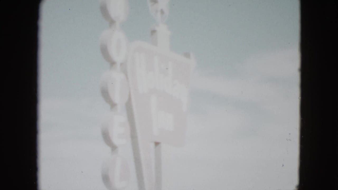Soft, overexposed view of vertical motel sign letters against the sky.