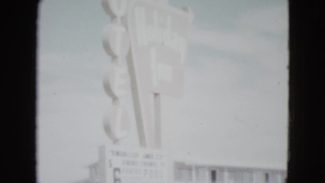 Motel sign with rate board beginning to appear above a two-story building.