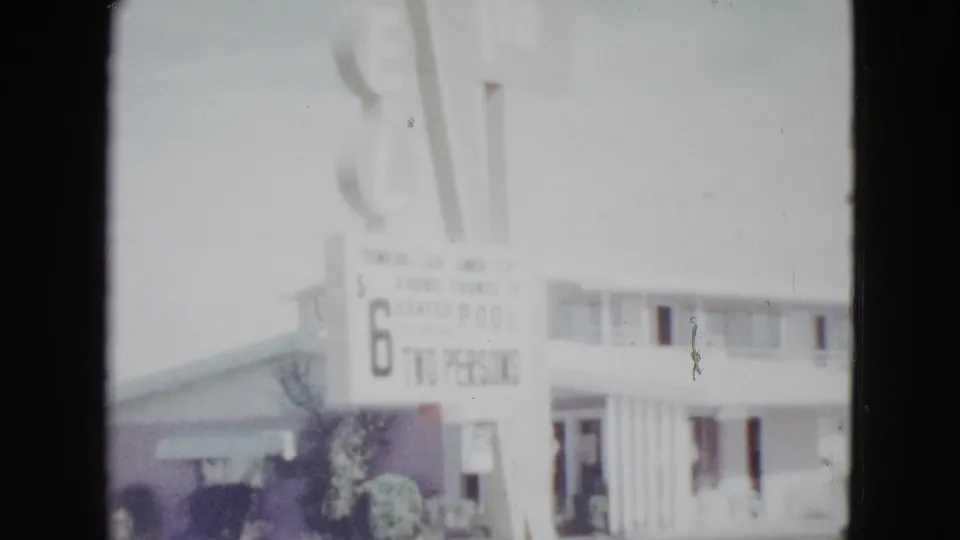 1958 Las Vegas home-movie frame showing a motel rate board advertising 6 dollars for two persons above the building.