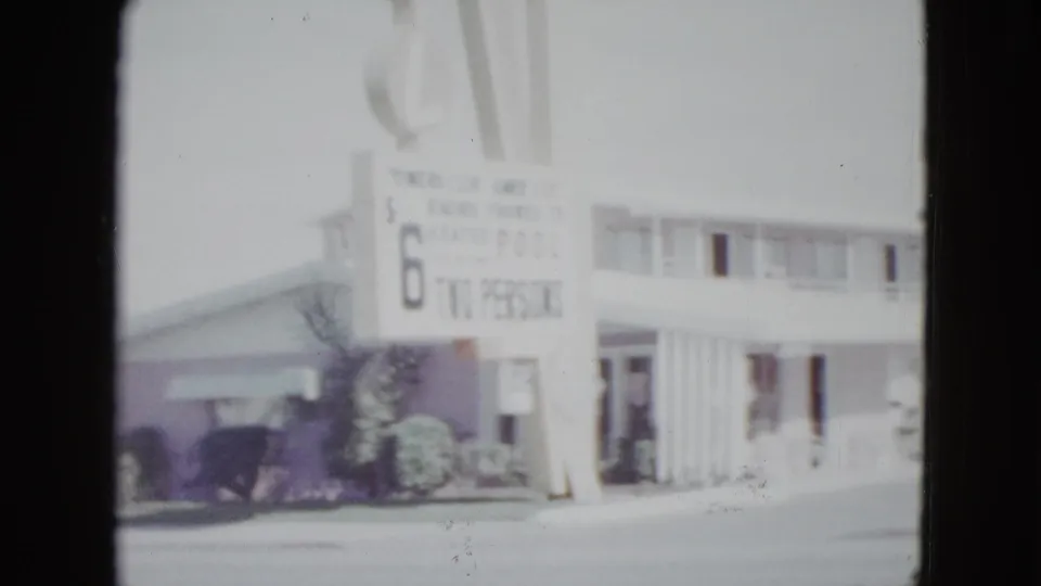 1958 Las Vegas frame showing the Holiday Inn sign, rate board, two-story motel exterior, shrubs, and street frontage.