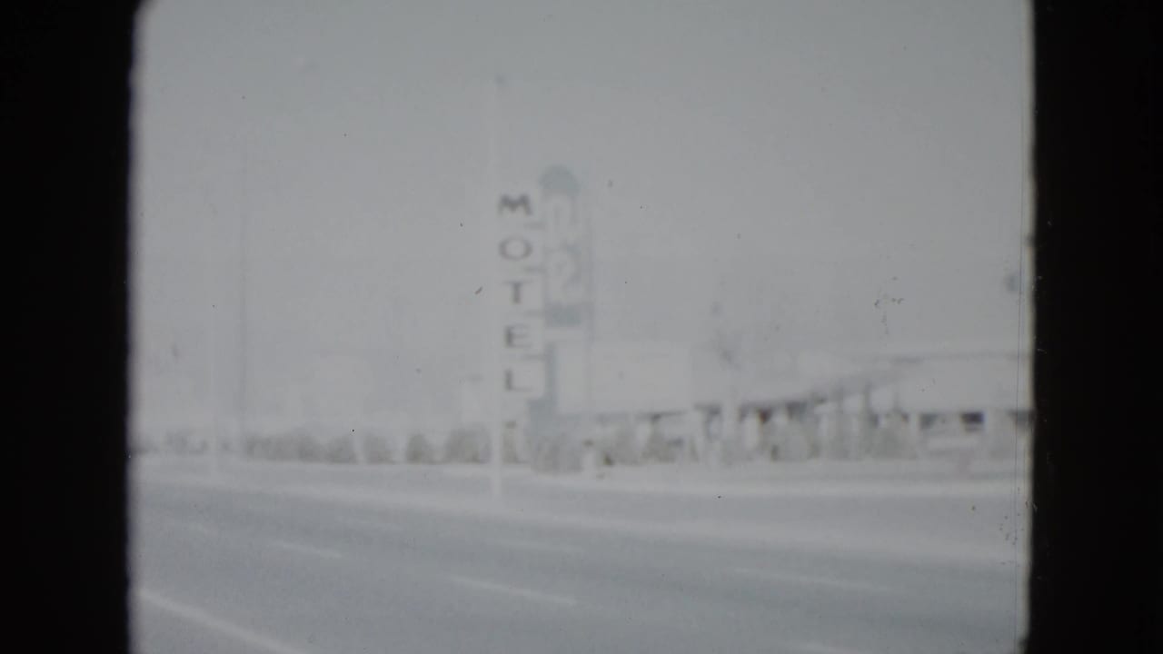 1958 Las Vegas roadside view with a tall vertical MOTEL sign, low commercial buildings, roadway, and faded 8mm exposure.