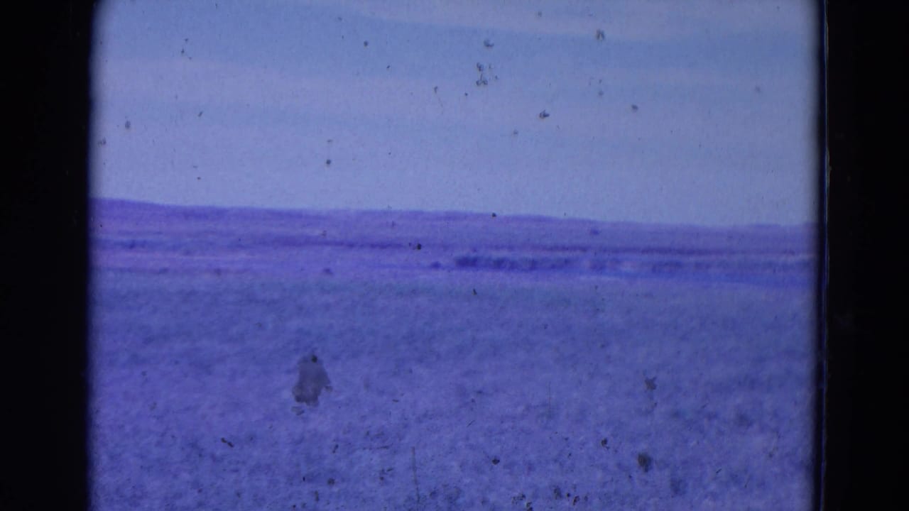 Metadata-listed 1958 Omaha 8mm frame with a low distant horizon, open blue-purple terrain or water, and visible film dirt.
