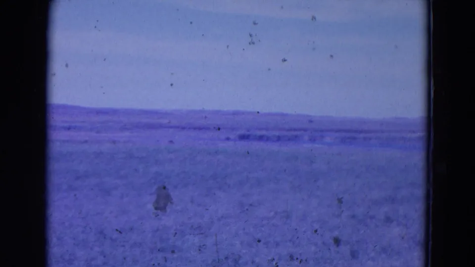 Metadata-listed 1958 Omaha 8mm frame with a low distant horizon, open blue-purple terrain or water, and visible film dirt.