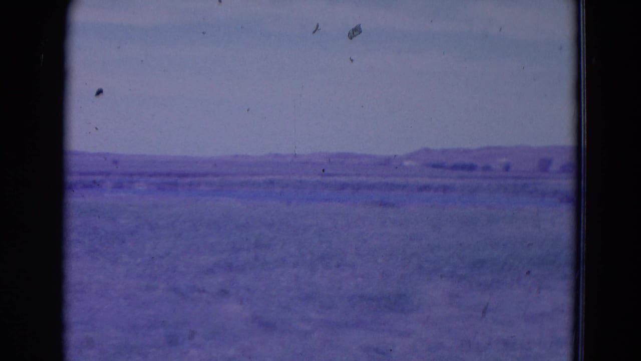 1958 Omaha, Nebraska-area landscape frame showing empty grassland, low hills on the horizon, and visible 8mm film artifacts.