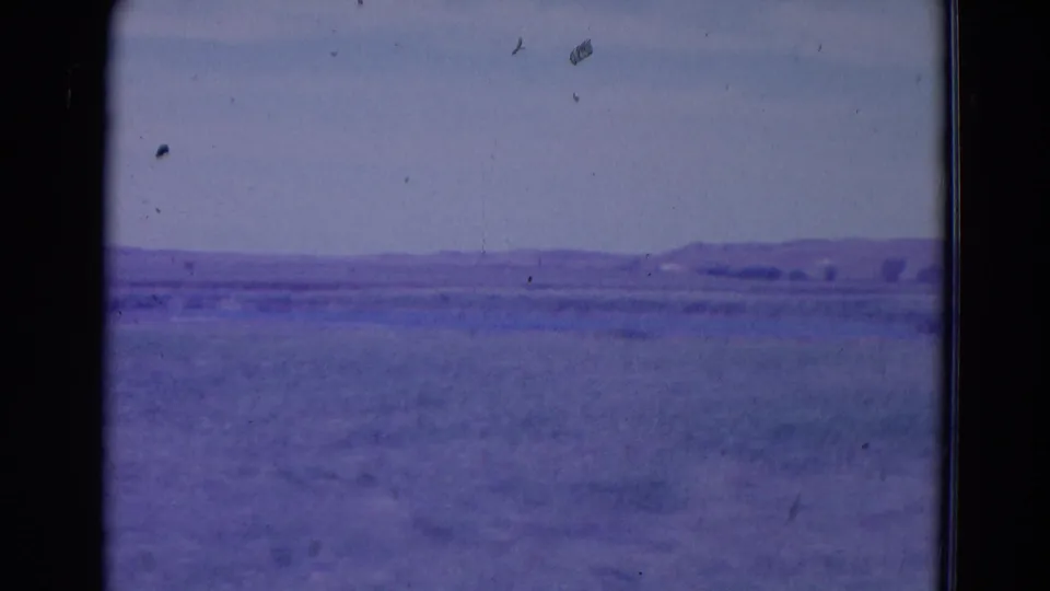 1958 Omaha, Nebraska-area landscape frame showing empty grassland, low hills on the horizon, and visible 8mm film artifacts.