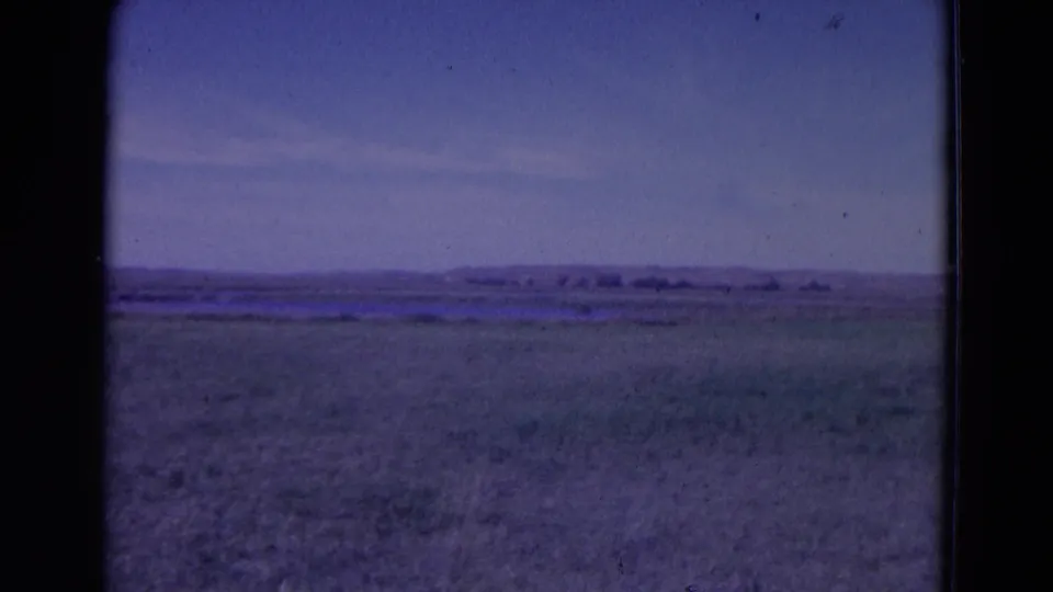 1958 8mm frame from the Omaha, Nebraska metadata showing open rural field, faint distant landforms, and blue-purple film color shift.