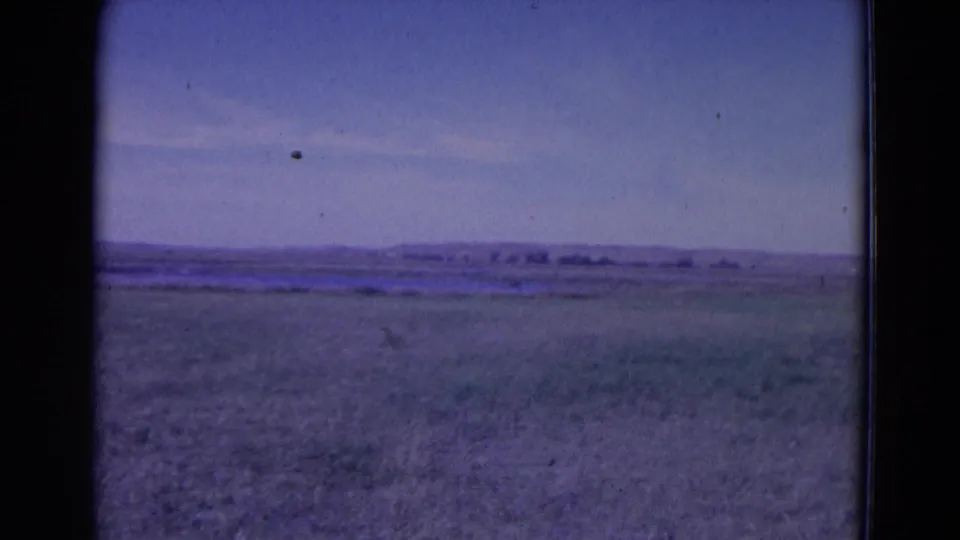 1958 Omaha, Nebraska-area home-movie still of empty grassy plain and low horizon, with soft 8mm texture and dust specks.