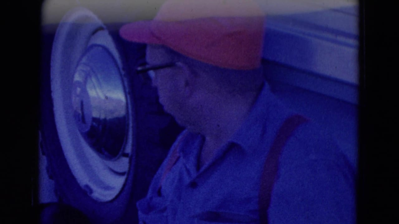 Man in red cap and glasses near a truck wheel with a strong blue film cast.