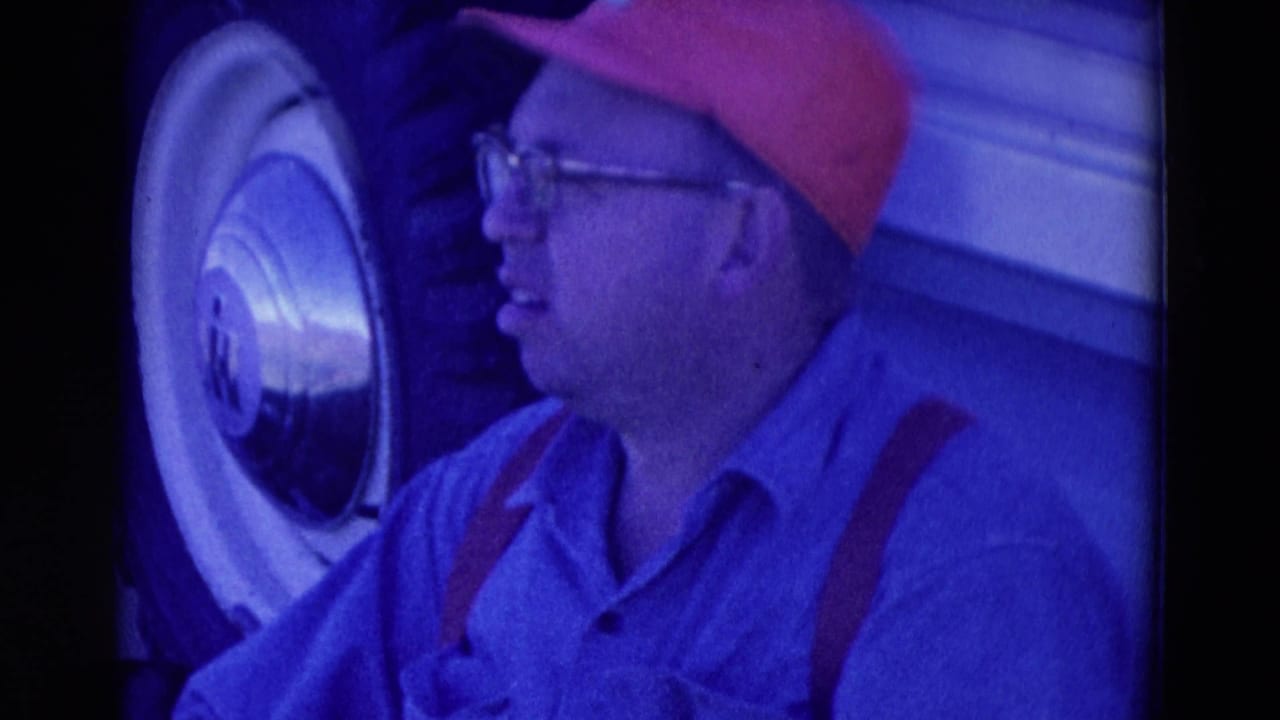 1958 Omaha frame of a man in glasses and red cap beside a whitewall truck tire and light-colored vehicle body.