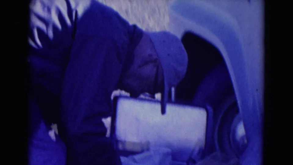1958 Omaha home-movie frame showing another man near the light-colored truck, holding a cup during the roadside stop.