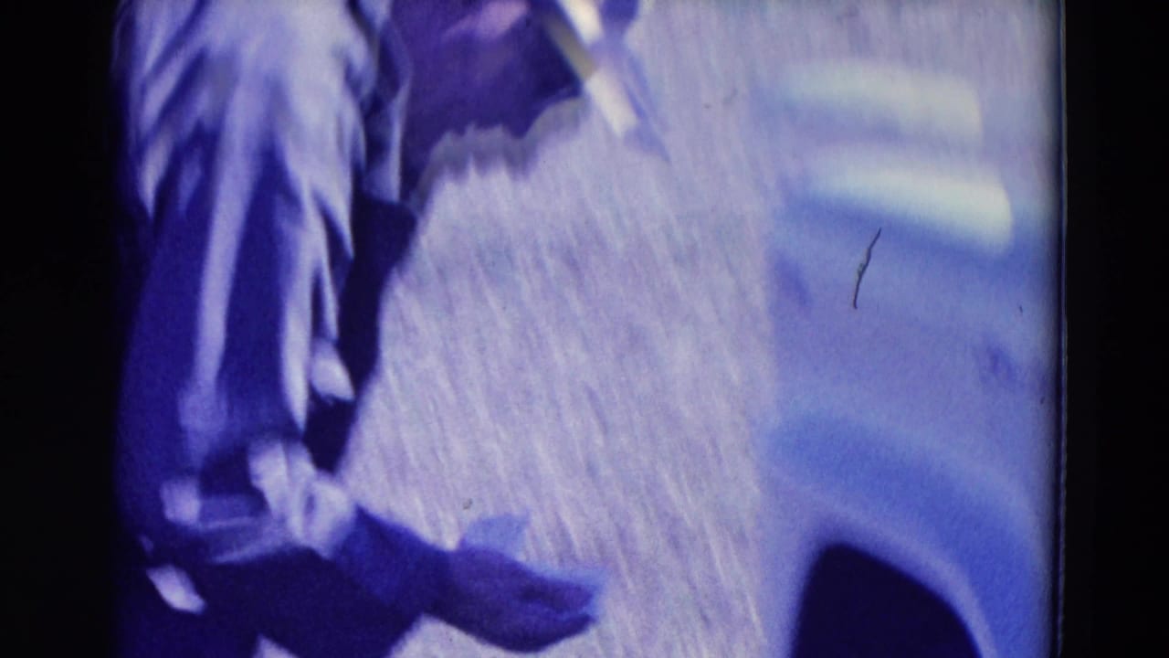 1958 Omaha home-movie frame showing a hunter's lower body near grass and a light-colored vehicle edge, with soft 8mm color shift.
