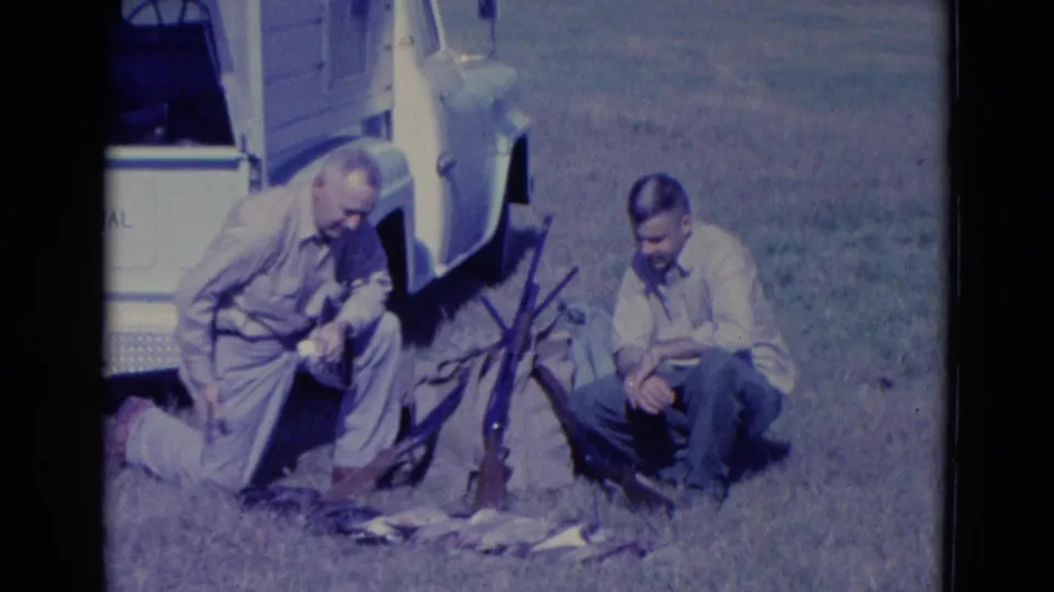 1958 Omaha-area 8mm frame showing two adult men in a grassy field beside a white pickup, with shotguns and harvested ducks visible.