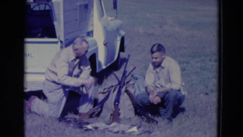 1958 Omaha-area hunting scene with one man kneeling over harvested ducks and another seated near shotguns beside a white truck.