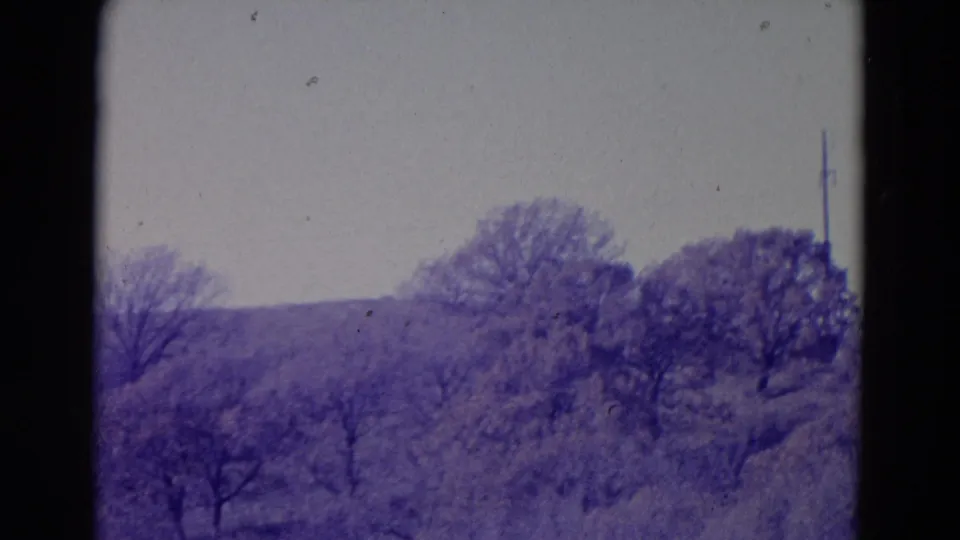 1958 8mm Omaha-area landscape frame showing open brush, bare-limbed trees, and a soft distant ridge under an overcast sky.