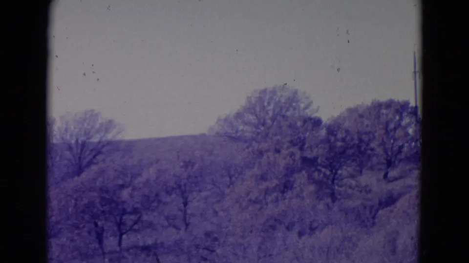 1958 Omaha-area 8mm frame showing leafless trees, brush, and distant low hills beneath an overcast sky.
