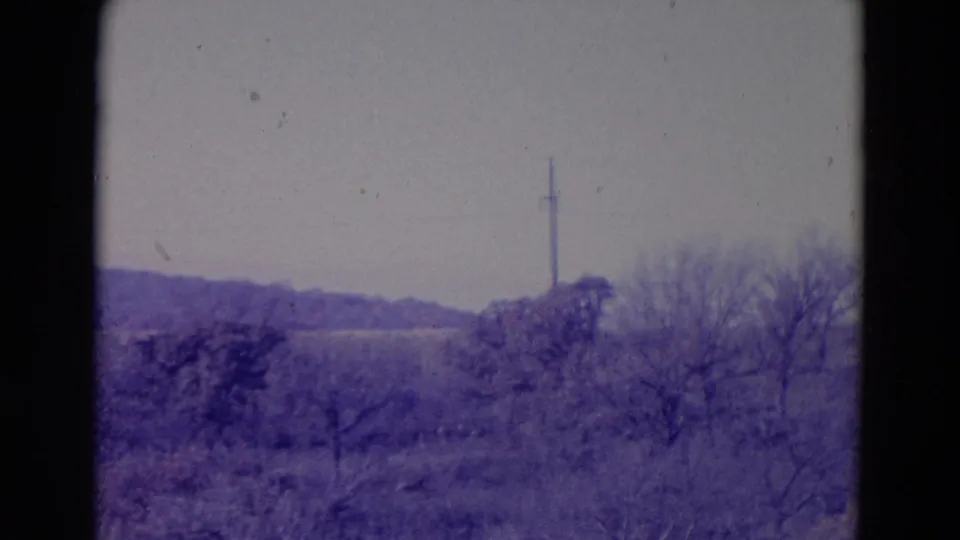1958 Omaha-area rural frame showing a tall utility pole in the distance beyond winter trees and open fields.