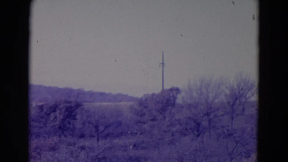 1958 Omaha-area 8mm frame with a distant utility pole, low fields, brush, and leafless trees in soft purple tint.