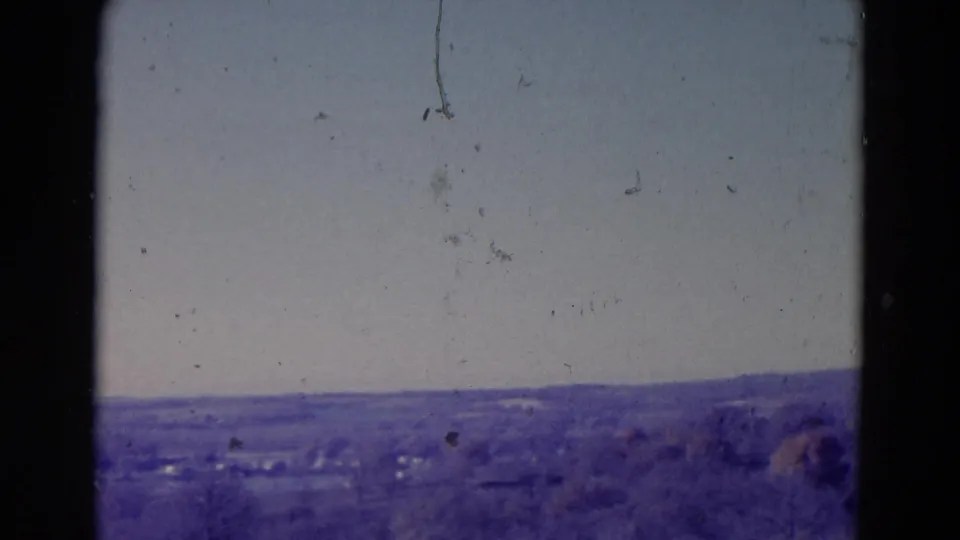 Omaha-area 1958 8mm frame with a wide pale sky, low rolling horizon, distant fields, and visible dust and marks from the film scan.