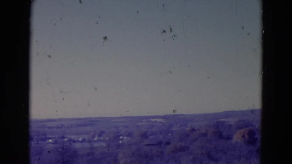 1958 Omaha-area home-movie frame showing a soft rural panorama with low hills, distant trees, and dark vertical framing edges.