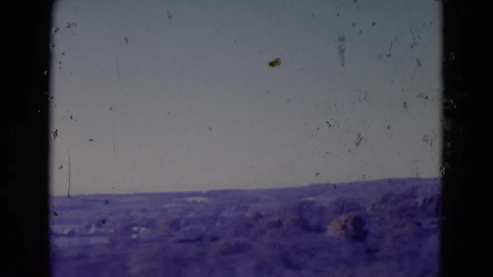 Omaha, Nebraska 1958 road-view frame with a muted horizon, distant vegetation, and aged 8mm dust and grain.