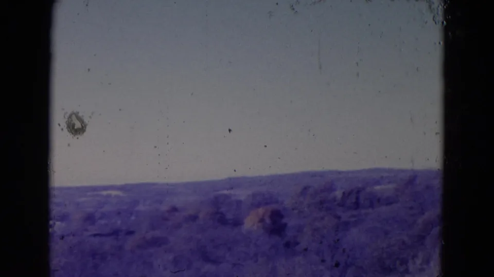 A 1958 home-movie view near Omaha shows low countryside and a broad sky, with dark framing and heavy aged-film texture.