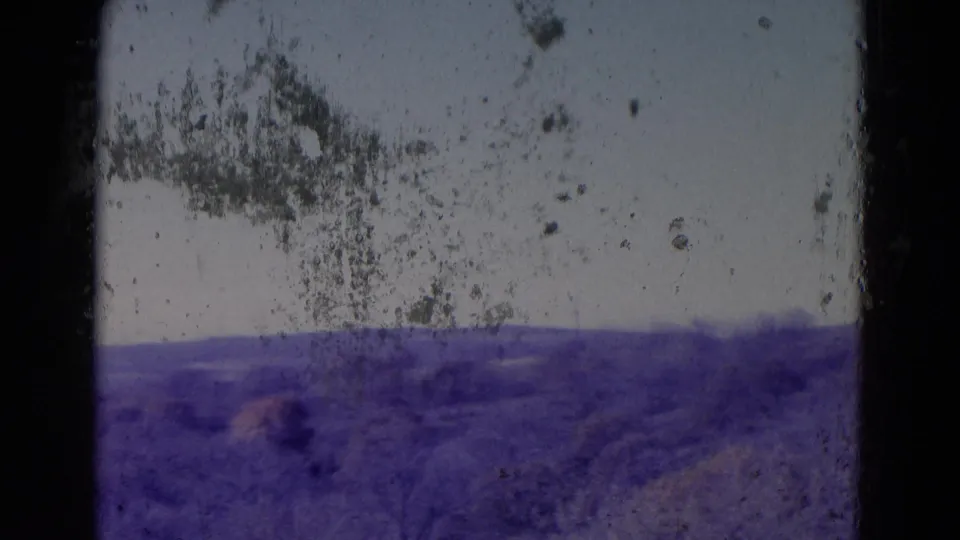 End frame of the Omaha-area 1958 rural view, with distant hills partly obscured by heavy dust, scratches, and color shift.